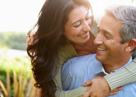 Smiling woman hugging smiling man from behind outdoors