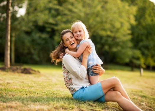 Mother hugging her daughter while sitting in grassy field