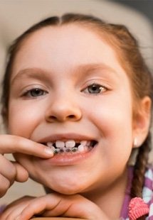 Child with orthodontics pointing to smile