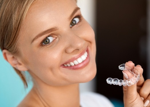 Woman smiling and holding clear aligner