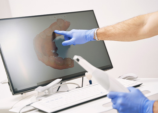 Dental professional pointing to models of teeth on computer monitor