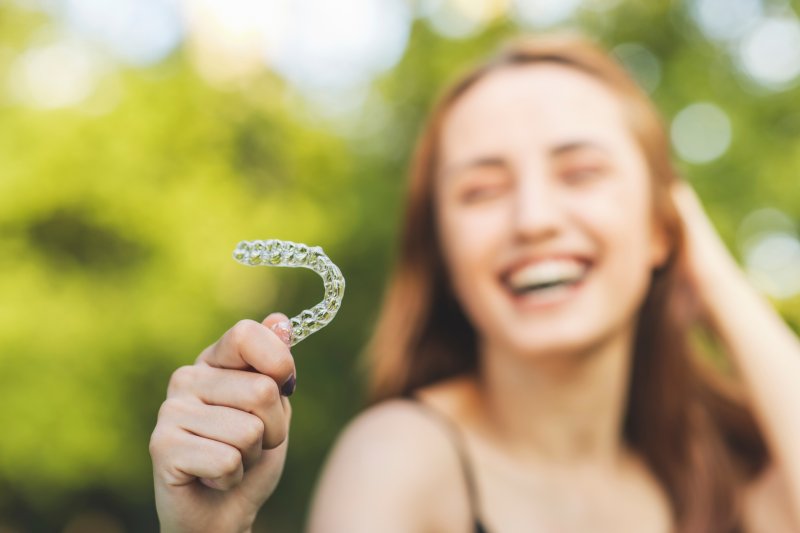 young woman holding her clear aligner in the sun